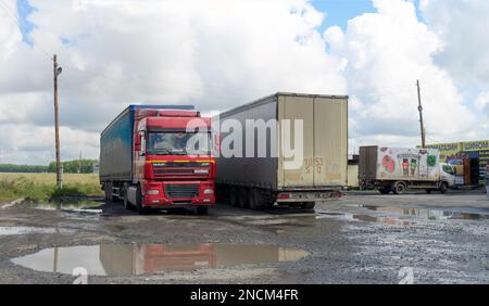 Large trucks MAN from Kazakhstan are resting, have puddles in the Parking lot at the cafe under the white clouds of a bright day Stock Photo