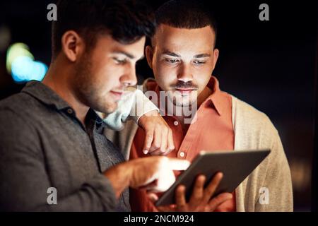 Theres so much to choose from online. two businessmen looking at a digital tablet while standing outside at night. Stock Photo