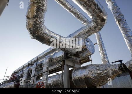 Details with industrial metallic pipelines covered in tin foil through which hot water flows. Stock Photo