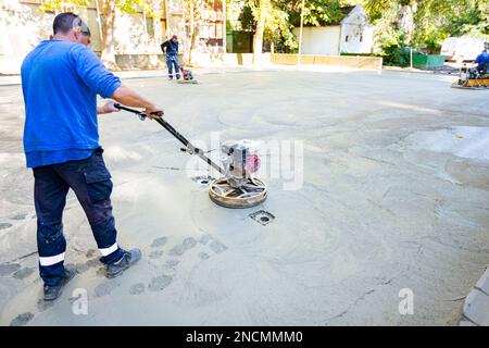 Worker using self-leveling power trowel machine with gas engine has wheels with pads, plate and he is driving it in circles smoothing surface on concr Stock Photo