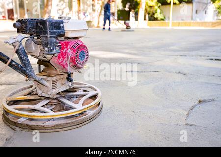 Worker using self-leveling power trowel machine with gas engine has wheels with pads, plate and he is driving it in circles smoothing surface on concr Stock Photo