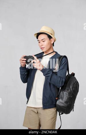 Young man carrying rucksack and using camera on white background Stock Photo