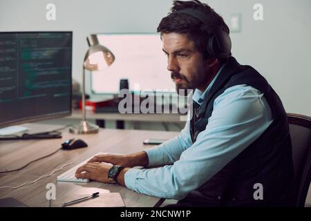 Headphones, programmer and man typing on computer, coding or programming at night. Information technology, thinking and male developer or coder Stock Photo