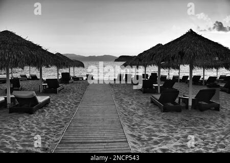 View of a wooden path leading to the stunning beach of Mylopotas in Ios Greece at sunset in black and white Stock Photo
