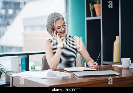 What time do you want to meet. a businesswoman making notes while talking on her cellphone. Stock Photo