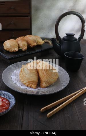 puffs filled with curried vegetables served on a wooden table against a black teaset background Stock Photo