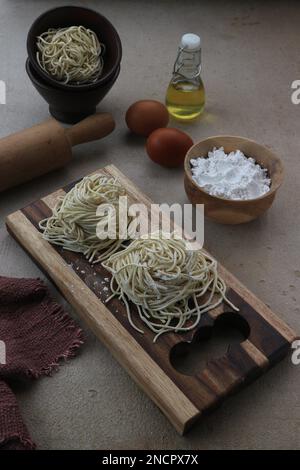 fresh noodles on a wooden tray with the ingredients of a bowl of flour, two eggs and palm oil Stock Photo