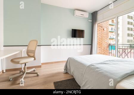 Spacious bright room with bed, large opening on entire wall with sliding plastic doors and access to balcony. Room has table with chair, air Stock Photo