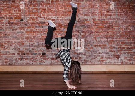 Dance is life. Happiness in moving. Sporty teenage girl, brick wall  background with free space. Hip hop lifestyle, flexible dancing young  female, breakdance concept Stock Photo