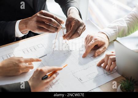 Close up of architects, engineers and designers sitting together at table and analysing blueprints. People of different ages and races working at office. Creation of construction project. Stock Photo
