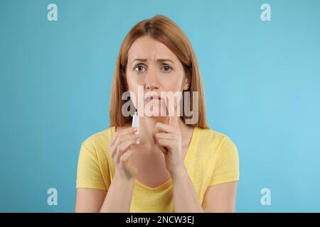 Upset woman with herpes applying cream on lips against light blue background Stock Photo