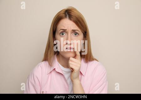 Upset woman with herpes applying cream on lips against beige background Stock Photo