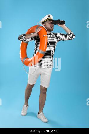 Sailor with binoculars and ring buoy on light blue background Stock Photo