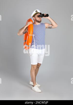 Sailor with binoculars and ring buoy on light grey background Stock Photo