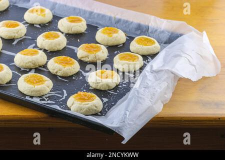 Half-cooked thumb print cookies filled with apricot jam on baking sheet. Selecive focus with copy space Stock Photo