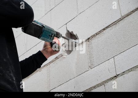 A man using a hammer to paint the brick wall of a building Stock Photo