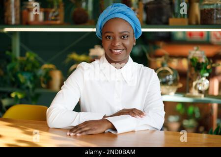 Beautiful cheerful young black woman sitting at cafe alone Stock Photo