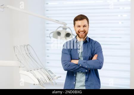 Confident male patient of stomatology standing in modern clinic. Man smiling at the camera crossing his arms in front of him. Stock Photo