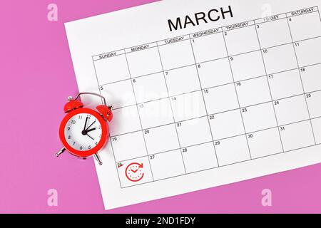Time change concept for Central European Summer Time on March 27th with red alarm clock and calendar sheet Stock Photo