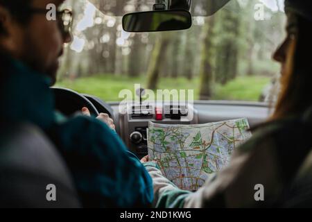 Smiling millennial caucasian couple in jackets riding in car in cold forest, enjoy adventurer, looking at map, cropped Stock Photo