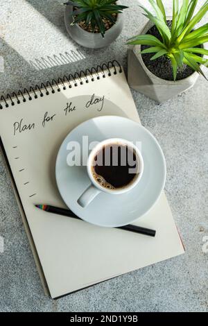 Plans for the day and morning cup of coffee on the table with green plants in the pot Stock Photo