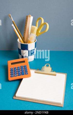 Pencil holder, calculator, memo clipboard on blue desk. business finance workspace Stock Photo