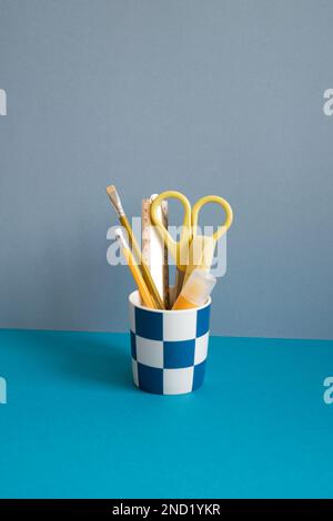 Yellow pencil, ruler, highlighter, scissors in holder on blue desk Stock Photo