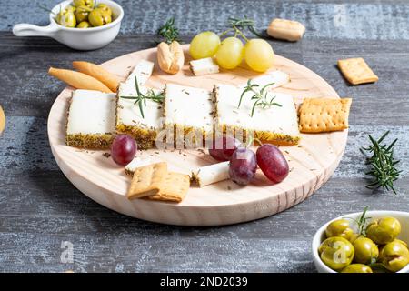 Appetizing cheese served on wooden table with ripe grapes and crackers decorated by rosemary sprigs near olives in bowls on table Stock Photo