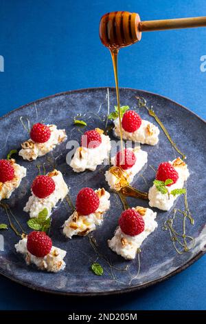 Unrecognizable chef serving plate with cream and raspberries decorated with mint leaves and nuts with honey Stock Photo