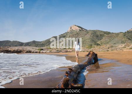 Distant image of female tourist in casual clothes walking on shore near waving sea on beach on sunny day Stock Photo