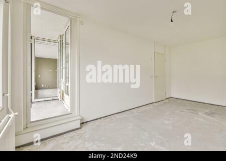 Interior of modern empty spacious room with white wall near window and concrete floor in residential building Stock Photo