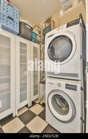 Interior of laundry room with modern washing machine and dryer stack placed near cupboard with plastic baskets on top Stock Photo