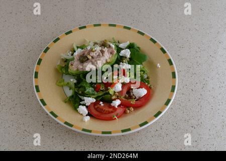 Avocado and Tuna Salad - 0n a bed of Rocket plus sliced tomatoes and Feta Cheese. Poor Man's Avocado Ritz!. On beige plate with yellow/green edging. Stock Photo
