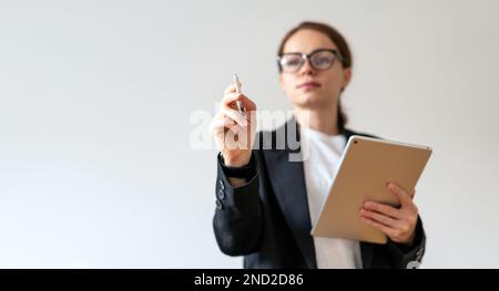Female researcher in background works in lab using digital pen signing work notes on virtual screen. Stock Photo