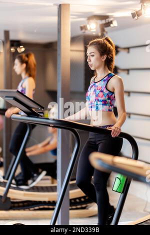 Fit girl exercising in modern fancy fithess studio. Side view of a woman walking on tredmill. Stock Photo