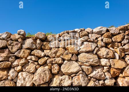 loosly stacked stone wall against a blue sky background Stock Photo