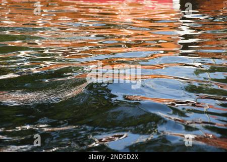 Reflections of colors on the surface of the water of a river, an orange boat is reflected creating an organic design. Stock Photo