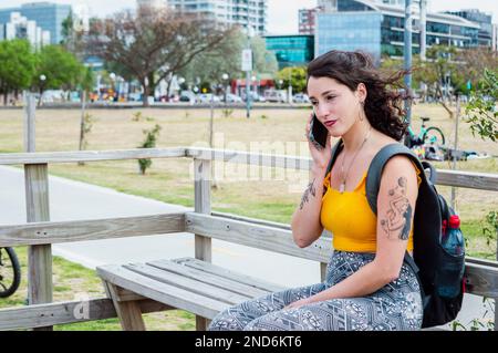 young latin traveler woman, sitting busy planning her trip over a phone call. Stock Photo