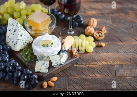 Cheese plate with grapes, honey, nuts and red wine on a wooden table. Stock Photo