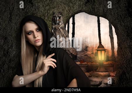 Witch wearing black mantle with owl in foggy forest. Fantasy world Stock Photo