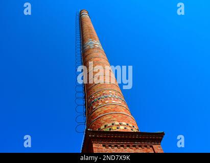 industrial brick chimney stack with steel access ladder and safety hoops. lightning rod and grounding device on the side. colorful enamel mosaic tiles Stock Photo