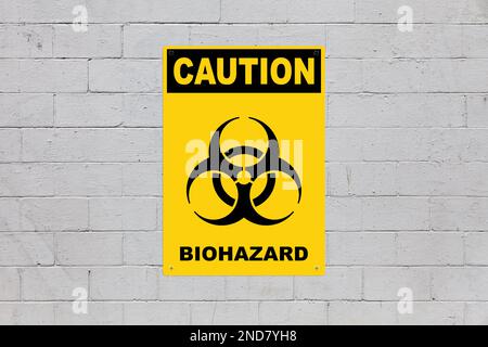 Yellow warning sign screwed to a brick wall to warn about a threat. In the middle of the panel, there is a biohazard symbol and the message is saying Stock Photo