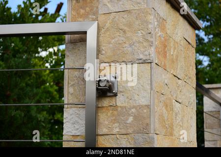 textured beige natural stone fence post or pier with stainless steel gate and hinge. welded square tube frame. twisted wire cable rail. landscaping. Stock Photo