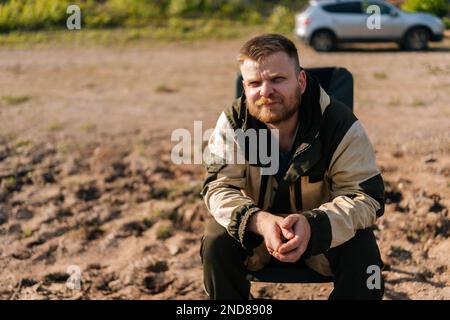 Premium Photo  Serious fisher male holding casting rod standing on bank  waiting for bites on water river at cloudy summer day looking at camera