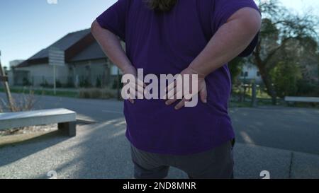 One overweight man suffering from back pain outside. A fat guy having lower chronic physical injury. Painful agony Stock Photo