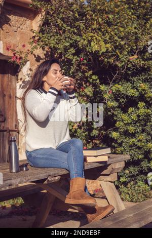 latin woman having a cup of coffee sitting on a wooden bench in the garden Stock Photo