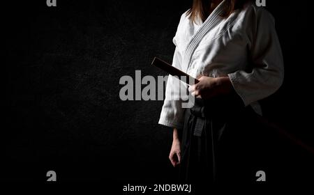 A woman in black hakama standing in fighting pose with wooden sword bokken over grunge dark background. Shallow depth of field. SDF. Stock Photo