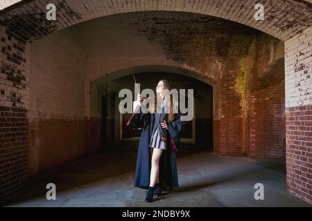 Young Woman Holding a Wand at the Entrance of a Dark Moody Corridor | Harry Potter | Gryffindor Stock Photo