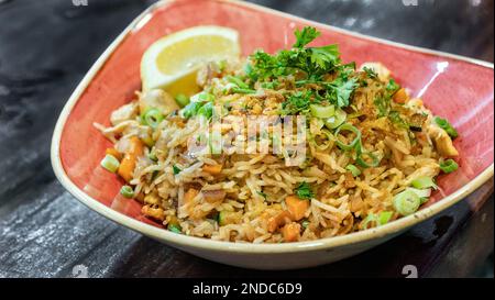 a bowl of freshly prepared oriental style prawn fried rice served in a red bowl with a lemon wedge Stock Photo
