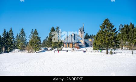 Sunny winter day at Kralovka Lookout and Mountain Hut, located near Bedrichov in the picturesque Jizera Mountains. Beautiful snowy landscape and cross-country skiers on the snowy plain below. Great outdoors and healthy winter activities in Jizera Mountains, Czech Republic. Stock Photo